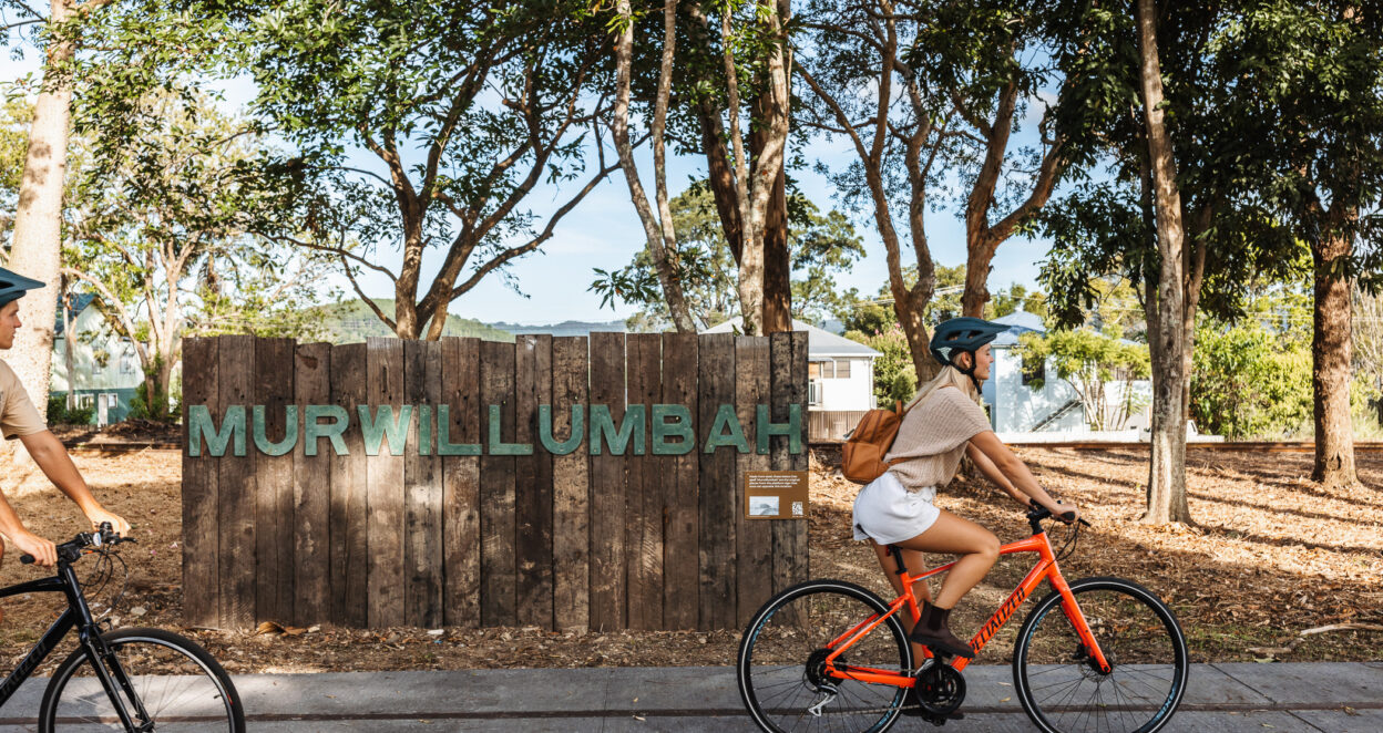 girl riding bike past murwillumbah sign